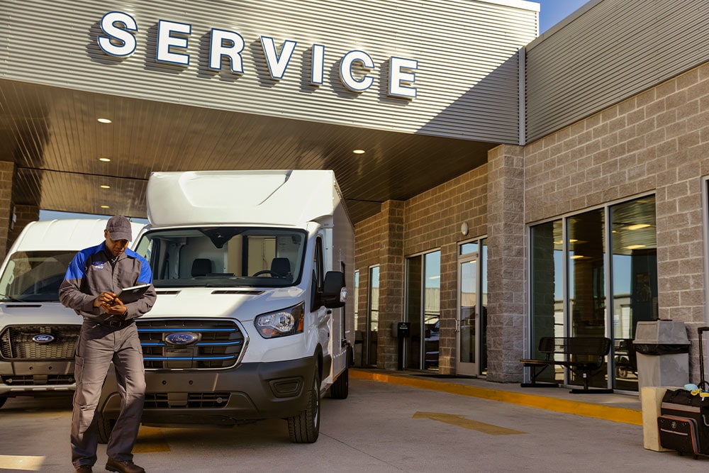 Ford mechanic standing in front of a white Ford van near a building labelled "service".