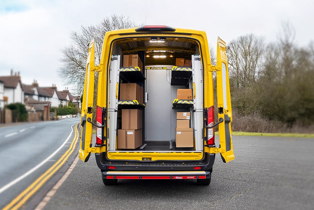 Rear view of a yellow Ford Transit van with open doors, revealing an organised interior with shelves and boxes.