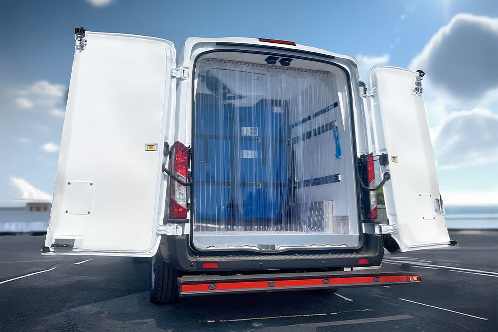 Rear view of a white Ford Transit refrigerated van with open doors and plastic strip curtains.