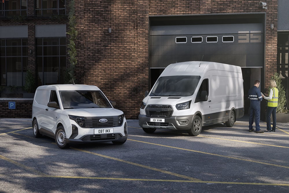 Two white Ford Transit vans parked in front of a modern building, two people chatting next to the vehicles.