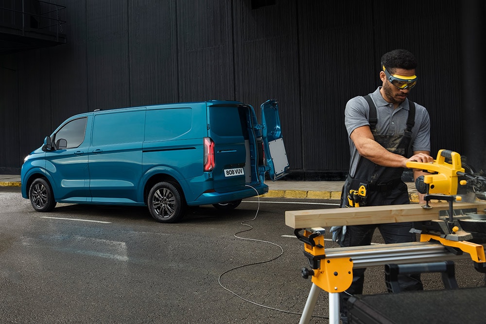 A carpenter working in the foreground, a blue Ford Transit parked in the background.