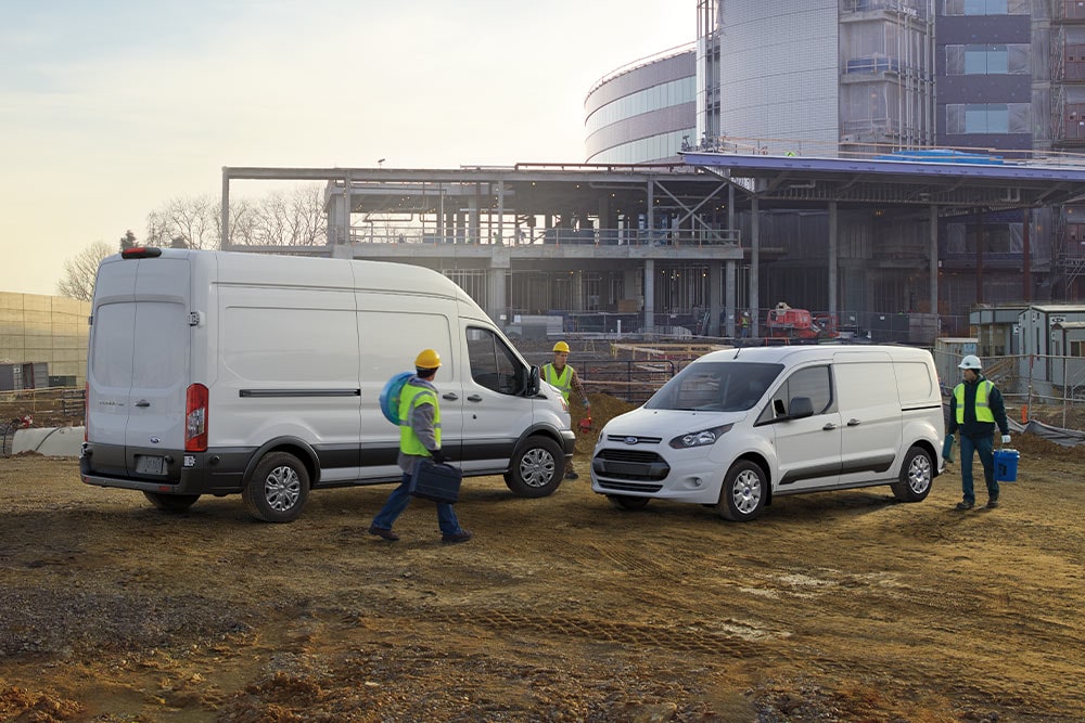Two white Ford vans parked at a construction site with workers walking around.
