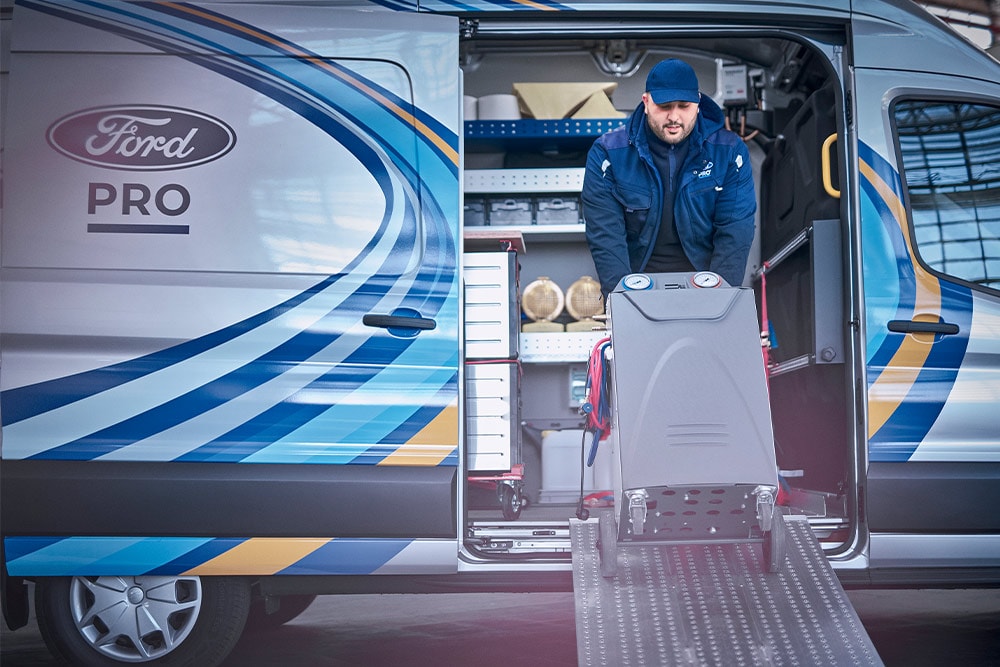 A Ford Pro mobile technician pulling tools out of a Transit van in front of a business.