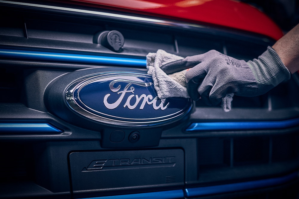 Close up of a technician polishing the Ford logo on the front of a red van.