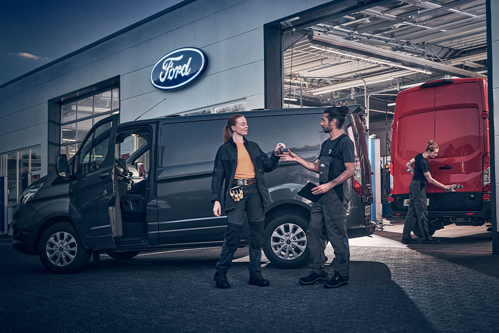 Customer and Ford technician exchanging keys for a van in front of a Ford dealership.