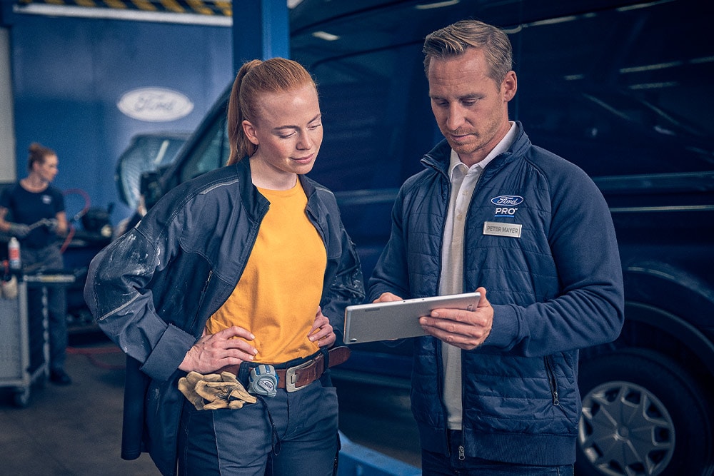 Ford technician and fleet manager reviewing data on a tablet in a garage.