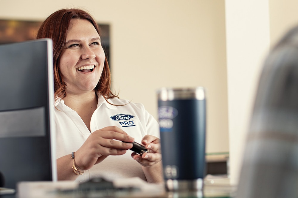 A person wearing a Ford Pro shirt smiles while holding a car key