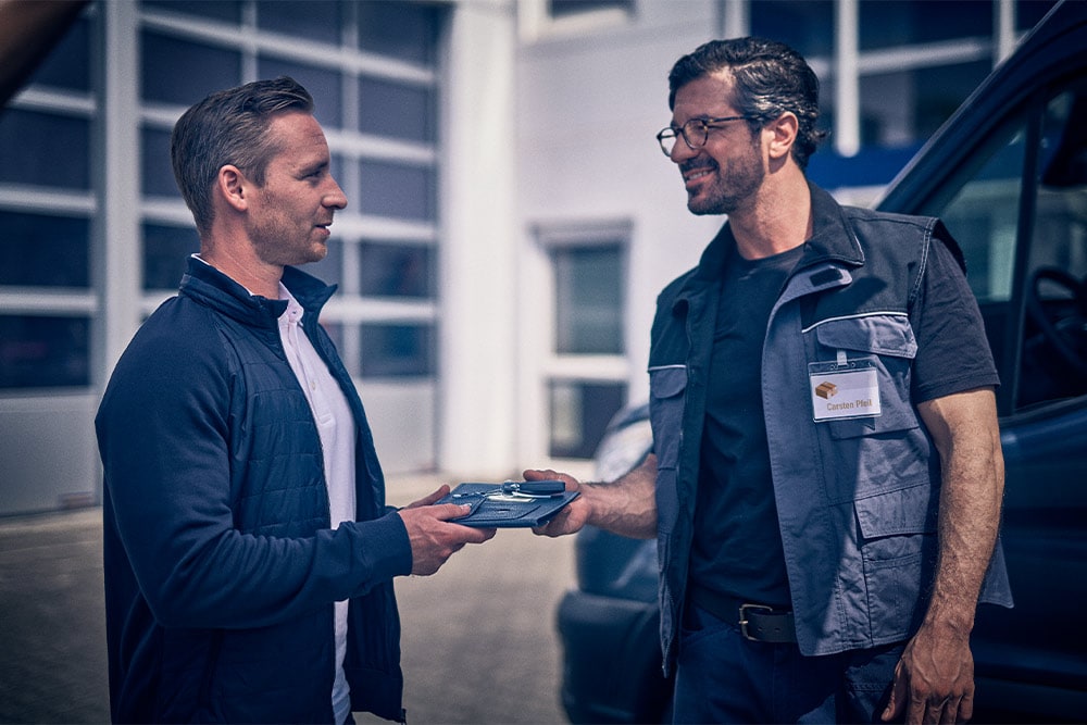 Two men shaking hands outside a Ford van, one handing over vehicle keys.