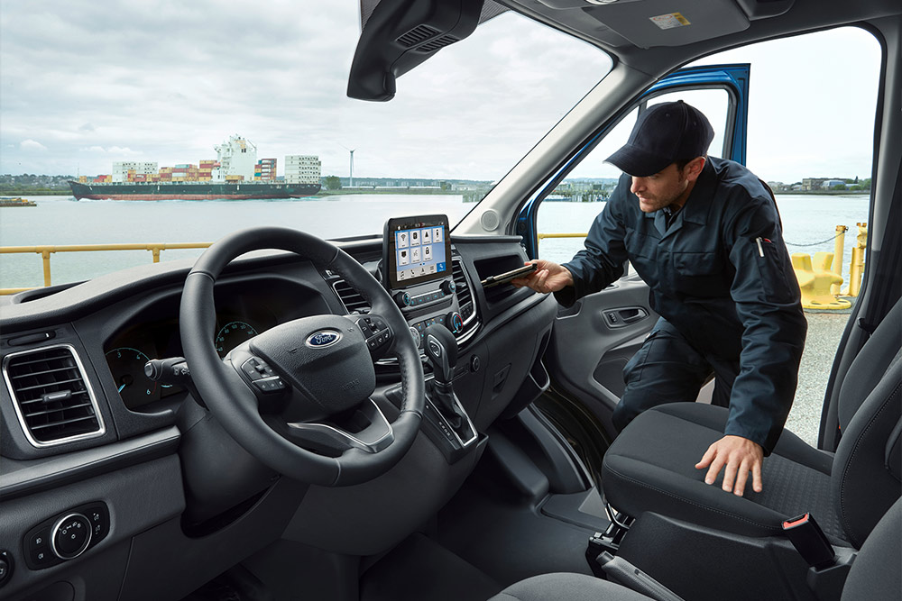 A man leaning into the open door of a Ford van, holding a phone, with a harbour in the background.