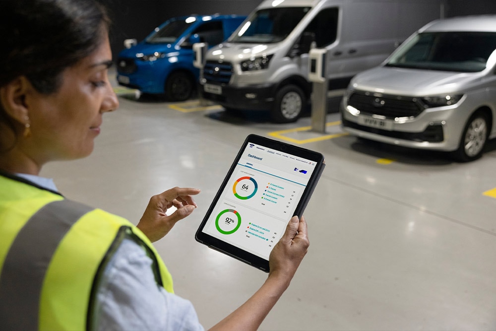 A person in a high-visibility vest holding a tablet displaying a dashboard with charts and data.