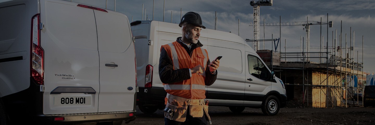 Service person with high viz jacket checking his phone with Ford Vans in background