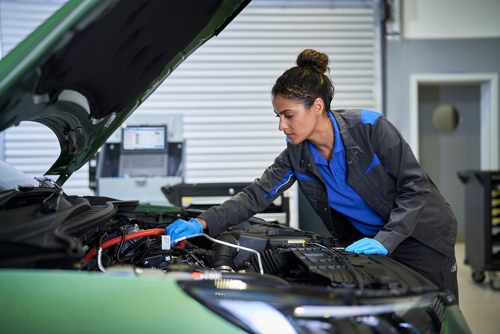 A Ford mechanic inspecting a car engine with its hood up in a garage.