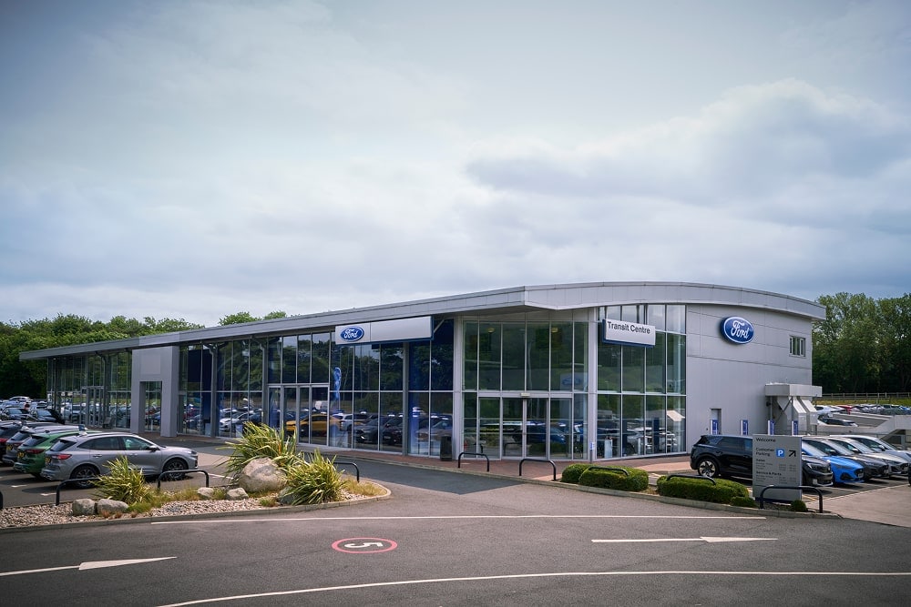 Outdoor view of a Ford car dealership with large glass windows. Cars are parked outside.