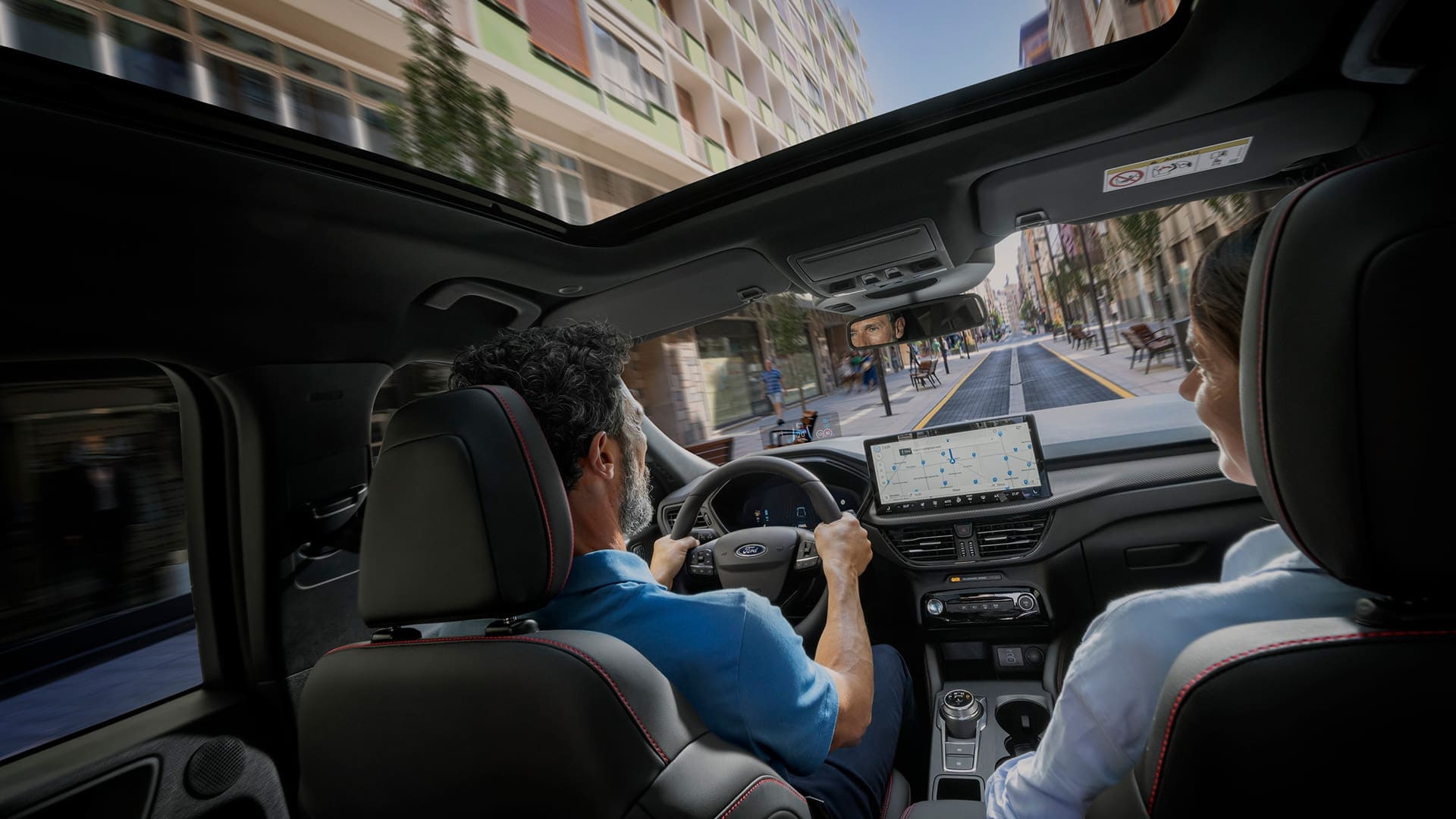 Passengers in a Ford vehicle with the SYNC digital screen displayed to help navigate a city route.