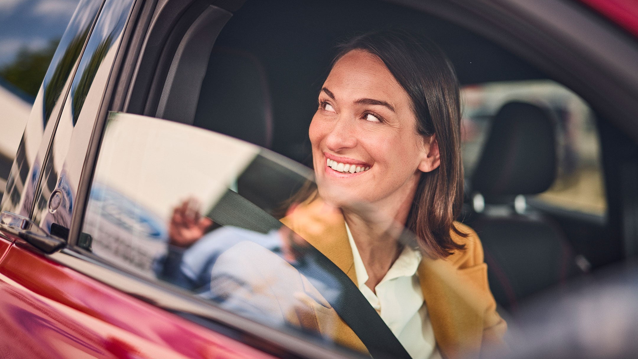 A person smiles while sitting in a red Ford car. 
