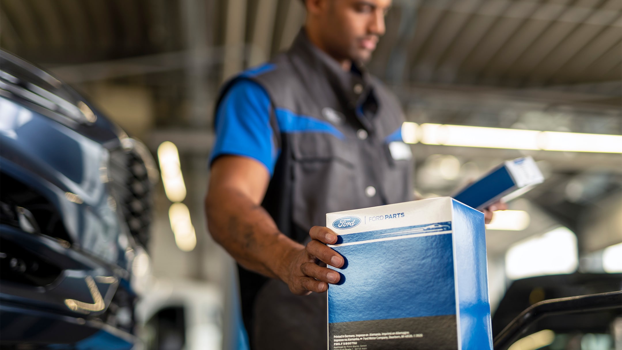 A mechanic at a Ford service centre holding a genuine Ford car part packaged in a branded box. 
