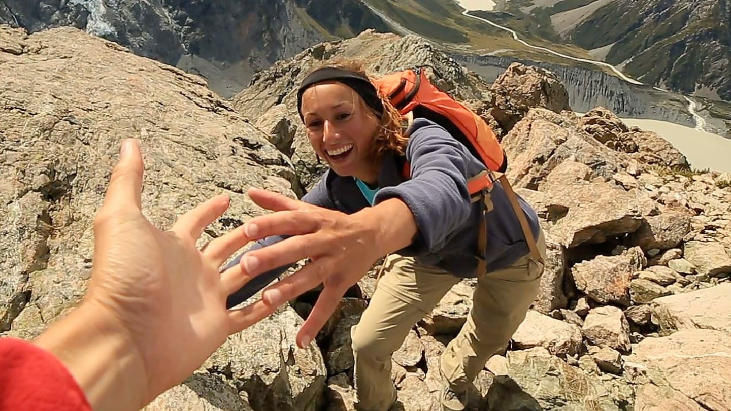 Hiker reaching for helping hand on rocky mountain ridge.
