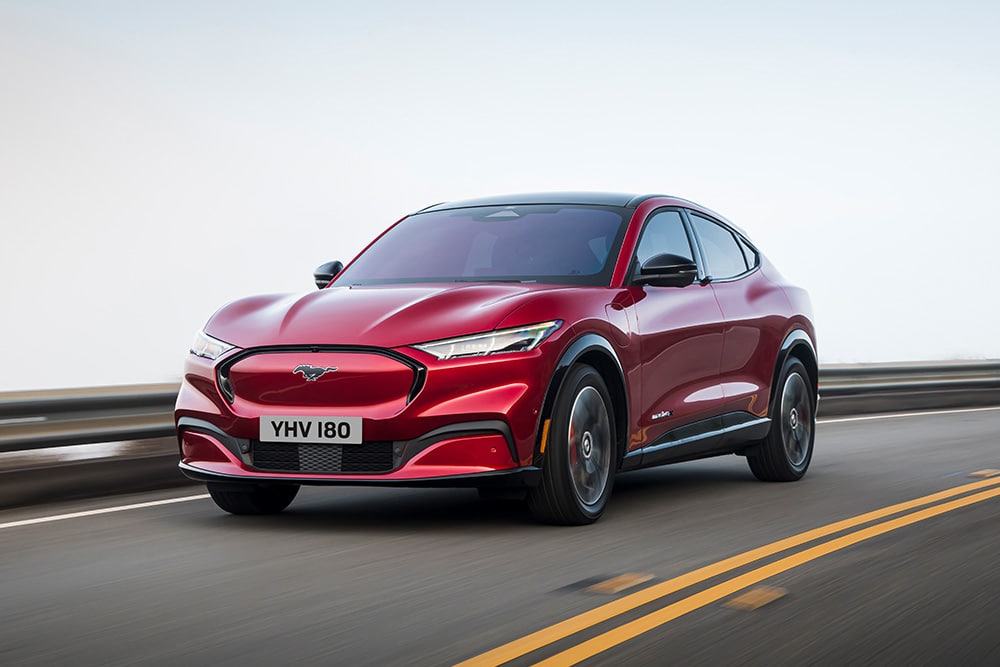 1000x667 image of a red Ford Mustang driving on a main road