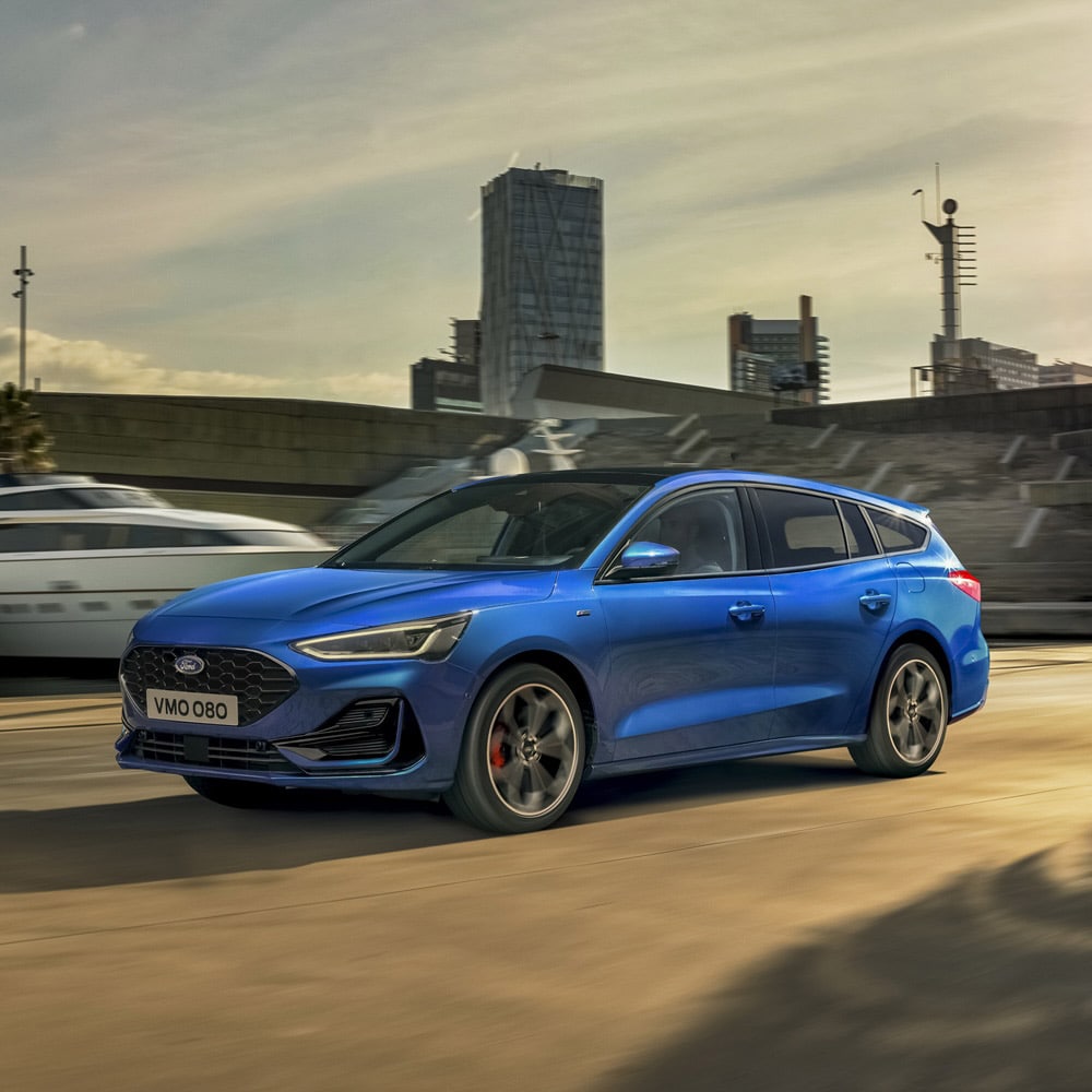 Blue Ford Focus: Front 3/4 view of a blue Ford Focus estate going through a city setting with a yacht.