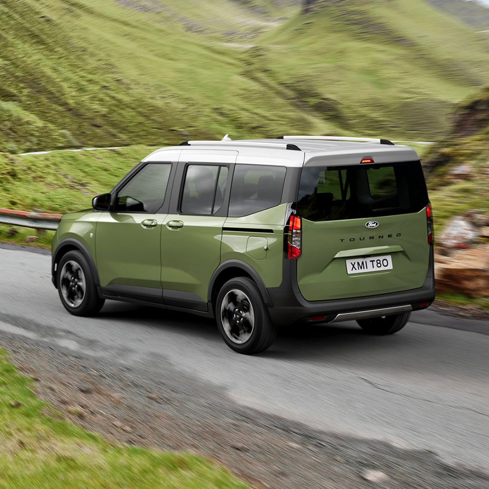 Rear 3/4 view of a green Ford E-Tourneo Courier driving on a winding road.