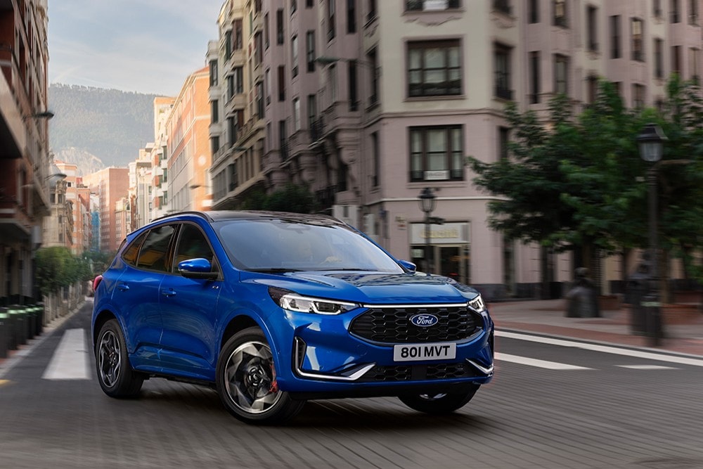 Blue Ford Kuga driving on a city street with buildings in the background.