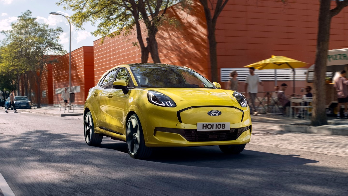 A yellow Ford Puma driving on a city street, with people in the background.