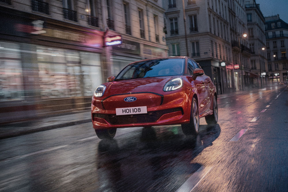 A red Ford vehicle driving on a wet city street at night, seen from the front three-quarter angle.