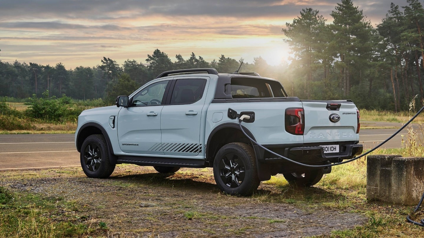 Ford Ranger Stormtrak PHEV charging, parked on a roadside with trees in the background.