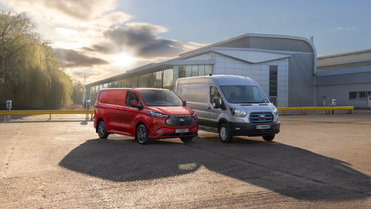 A red Ford E-Transit Custom and a silver Ford E-Transit parked in front of a building.