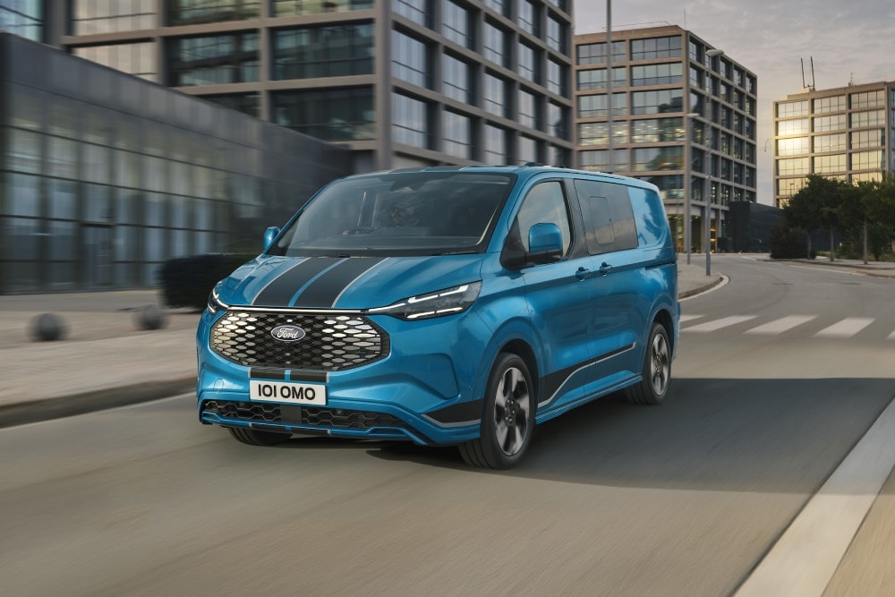 Current Promotions": Front 3/4 view of a blue Ford E-Transit Custom with black racing stripes driving on a city street.