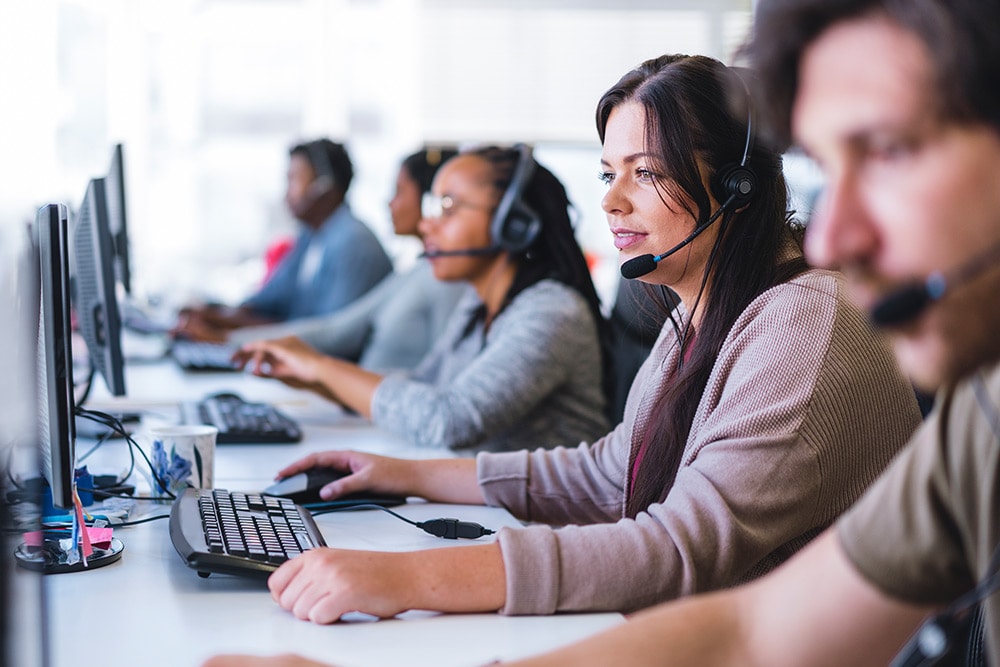 A group of people wearing headsets, working at computers in an office