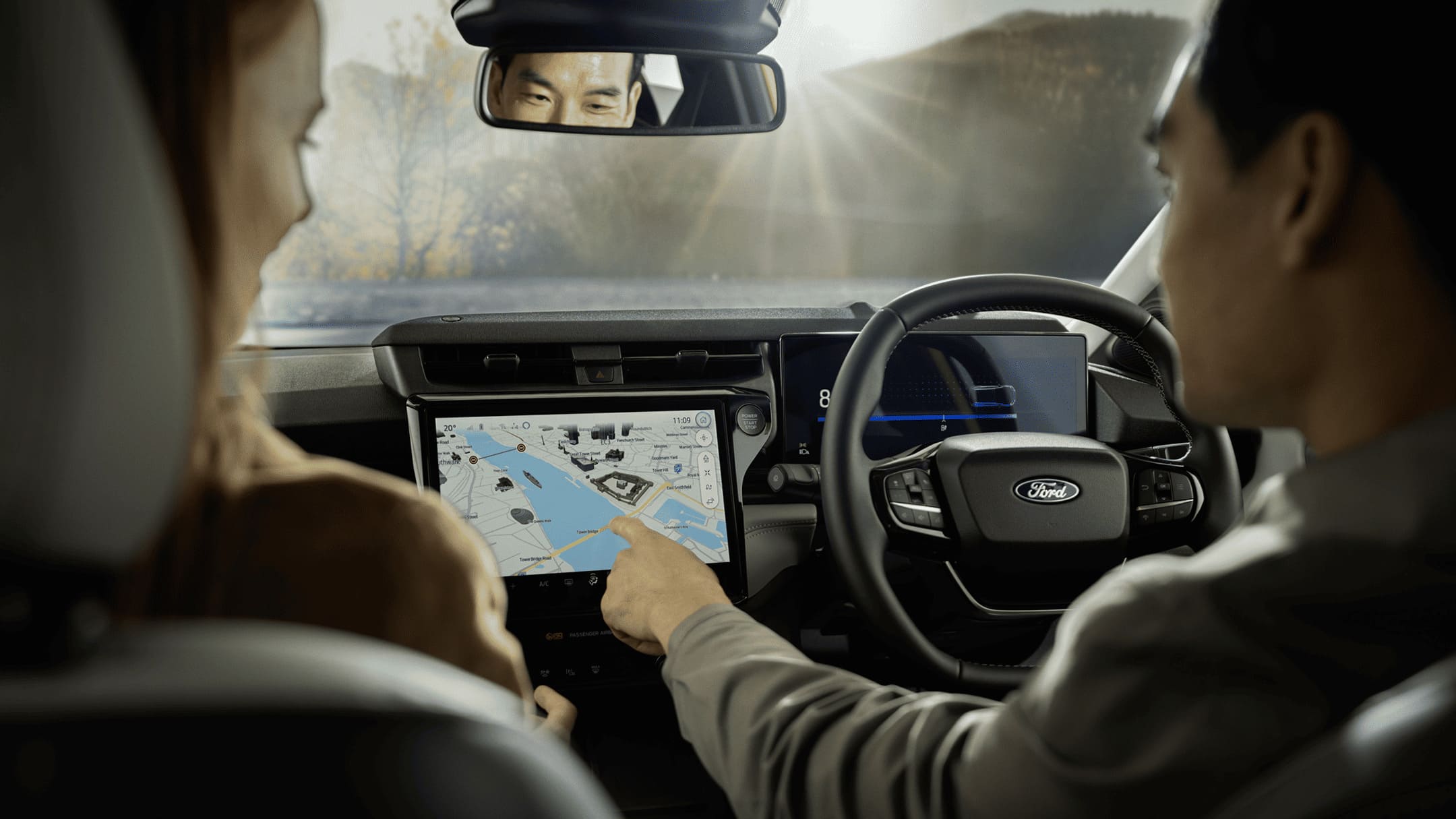 Interior of a Ford vehicle with a person pointing at a large touchscreen displaying a navigation map.