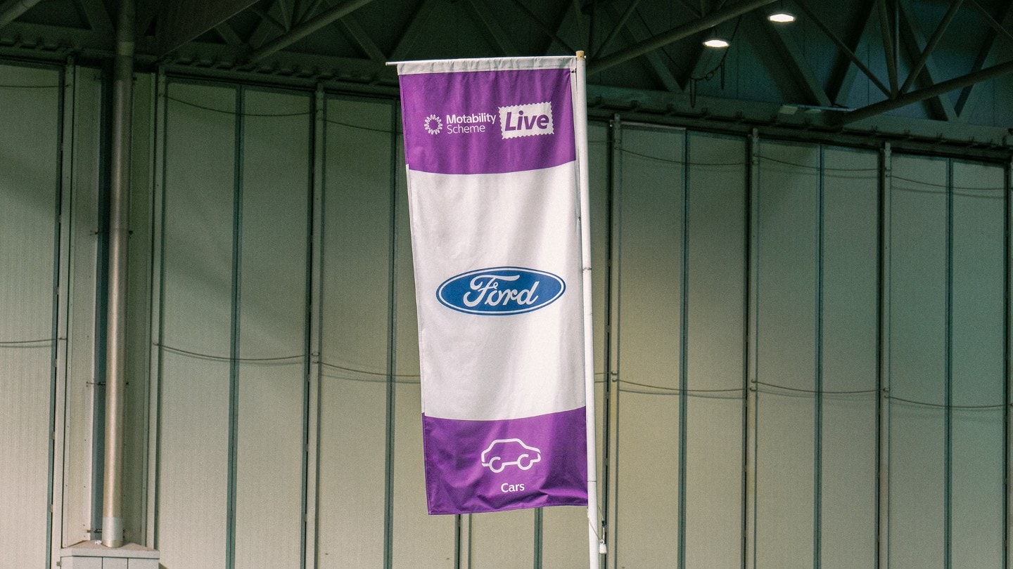A Ford flag featuring the Ford logo, “Motability Scheme Live" text, and a car icon.