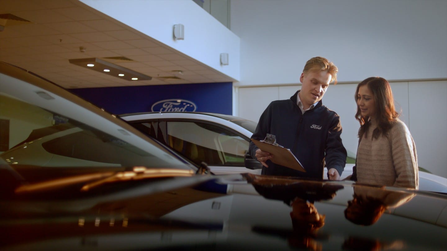 A Ford employee discusses vehicle options with a customer in a Ford showroom.