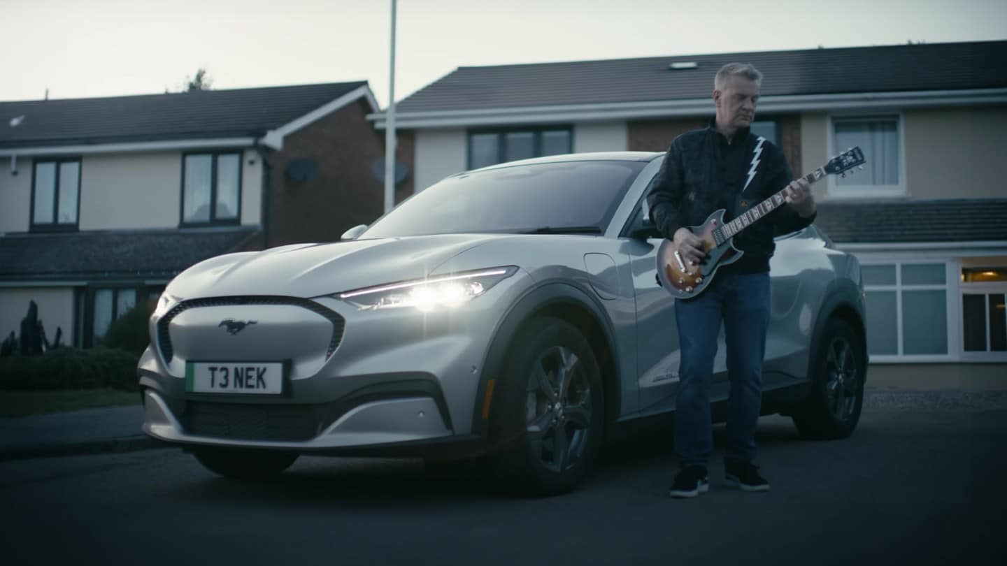 Musician Peter Steer stands with his guitar next to his Mustang Mach-E.