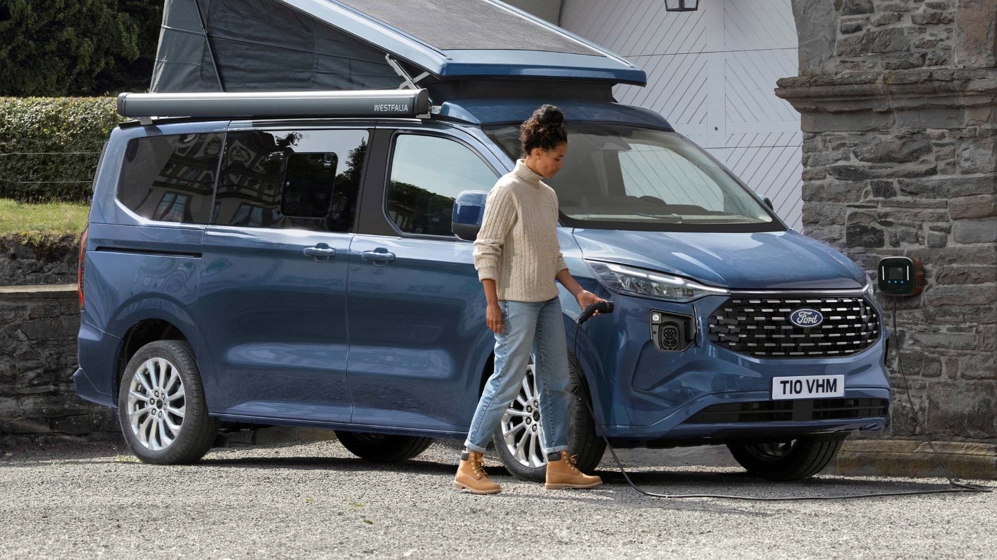 A woman plugs a charger into the All-New Plug-in Hybrid Custom Nugget Camper.