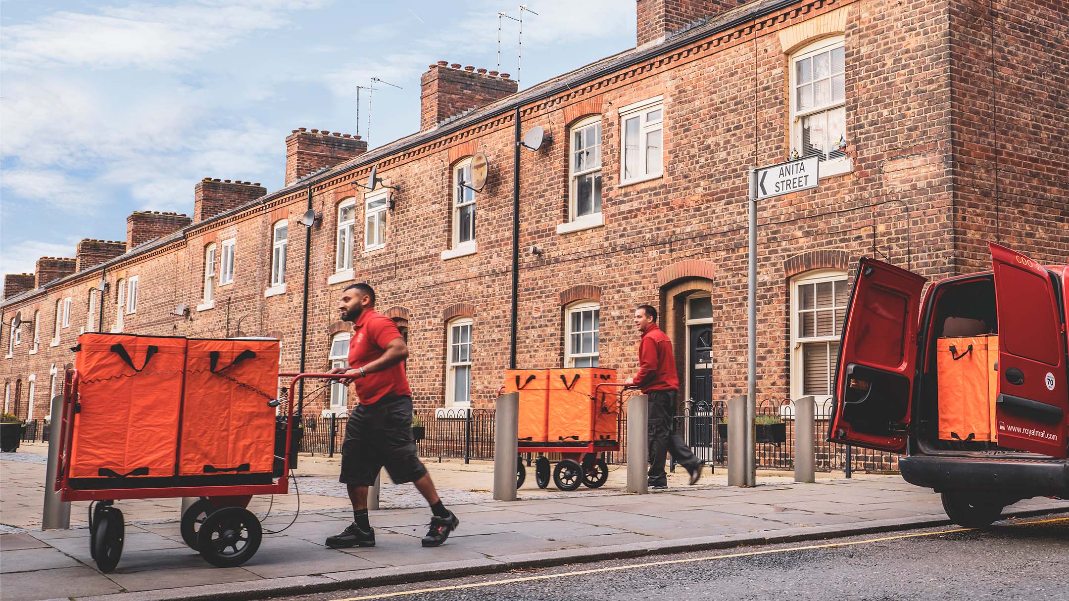 Two men in red T-shirts pushing trolleys with packages