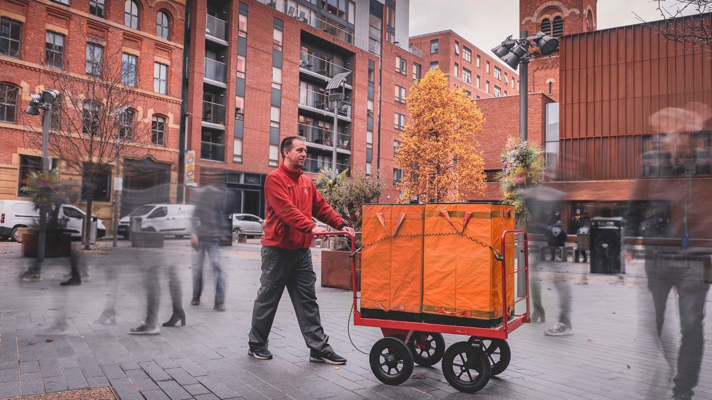 Man pushing a trolley with a package through a square