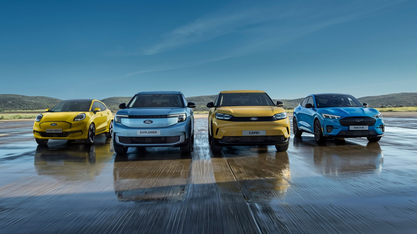Four Ford EVs: Yellow Puma Gen-E, blue Explorer, yellow Capri, and blue Mustang Mach-E, lined up on a wet surface.