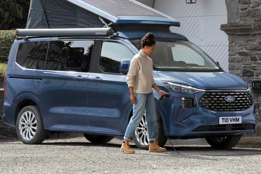 A woman plugs a charger into the All-New Plug-in Hybrid Custom Nugget Camper.