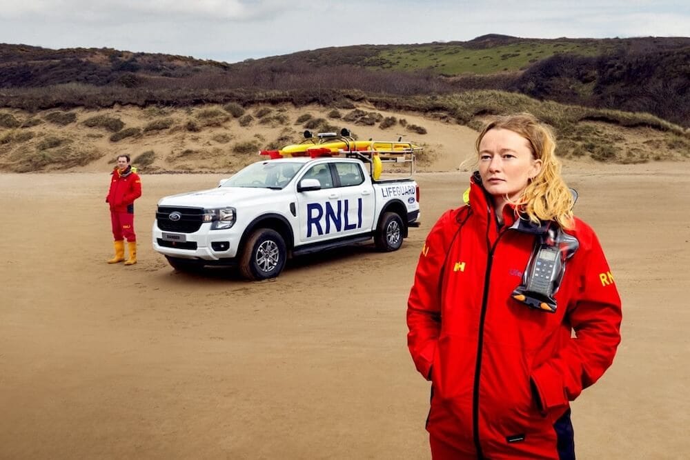 RNLI lifeguards standing besides Ford Ranger parked on a beach