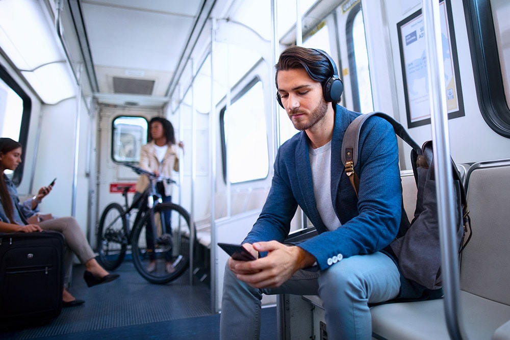 Young man sat on train with headphones looking at phone