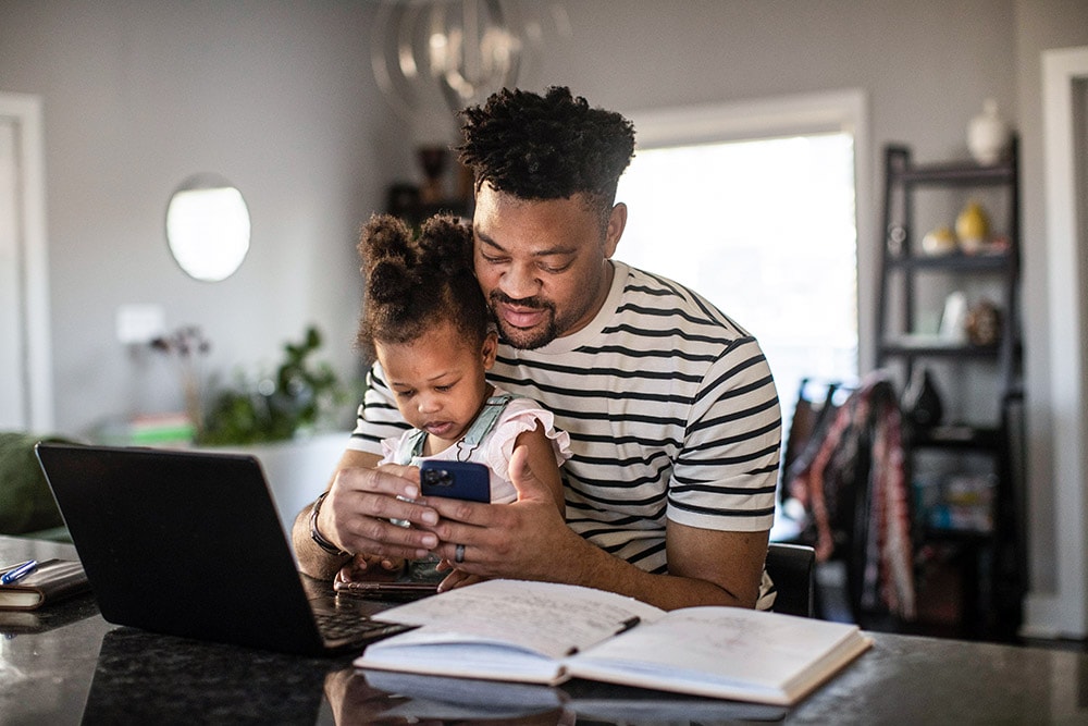 Man sitting with baby daughter at desk and looking at phone