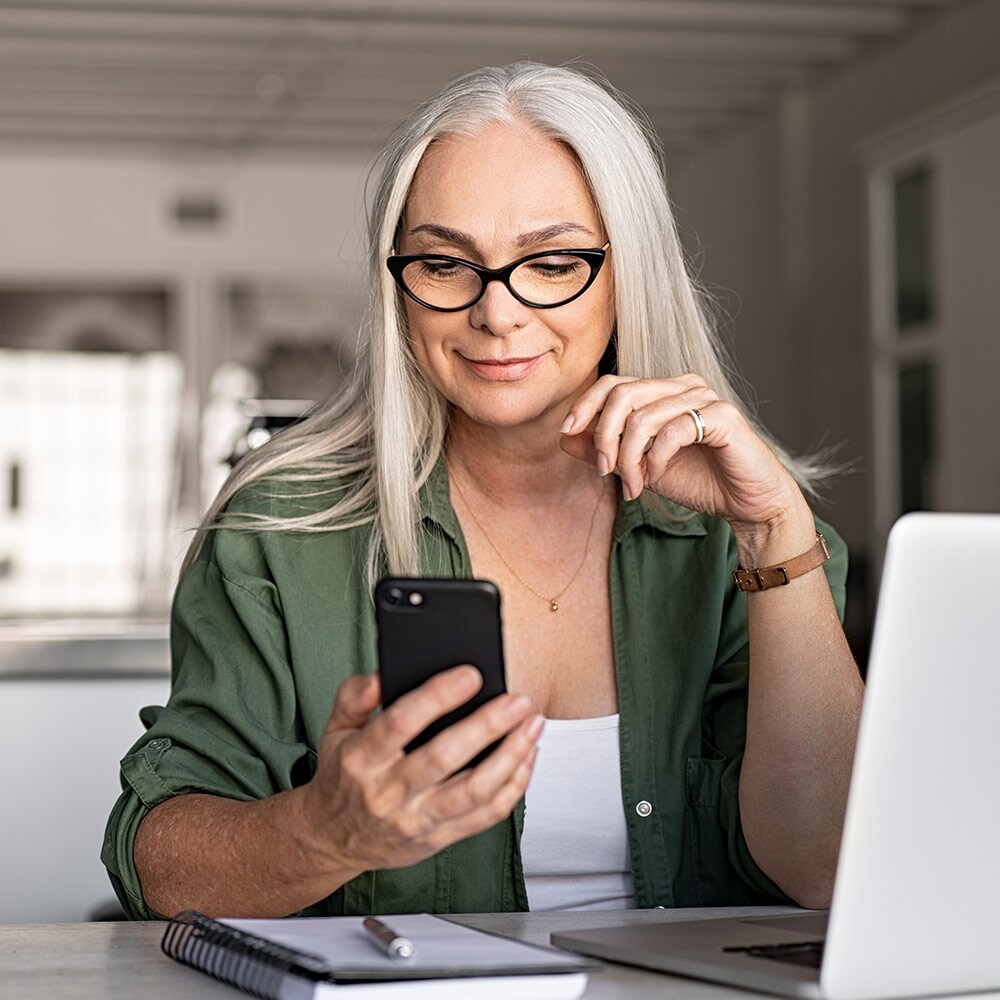 Older woman sat at desk and checking phone