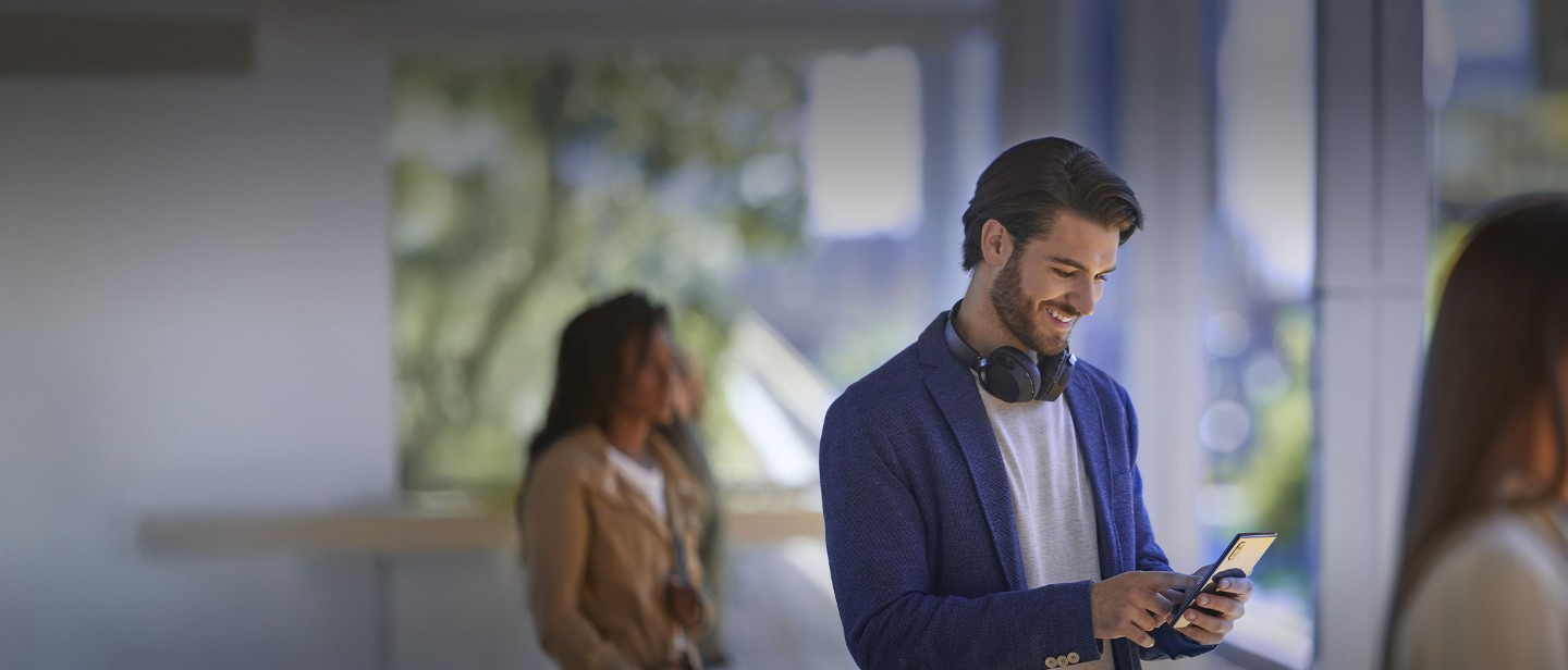 A person wearing headphones and a blue blazer looking at a mobile phone.