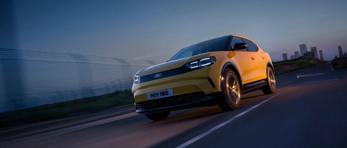 Yellow Ford Capri driving on a road at sunset.