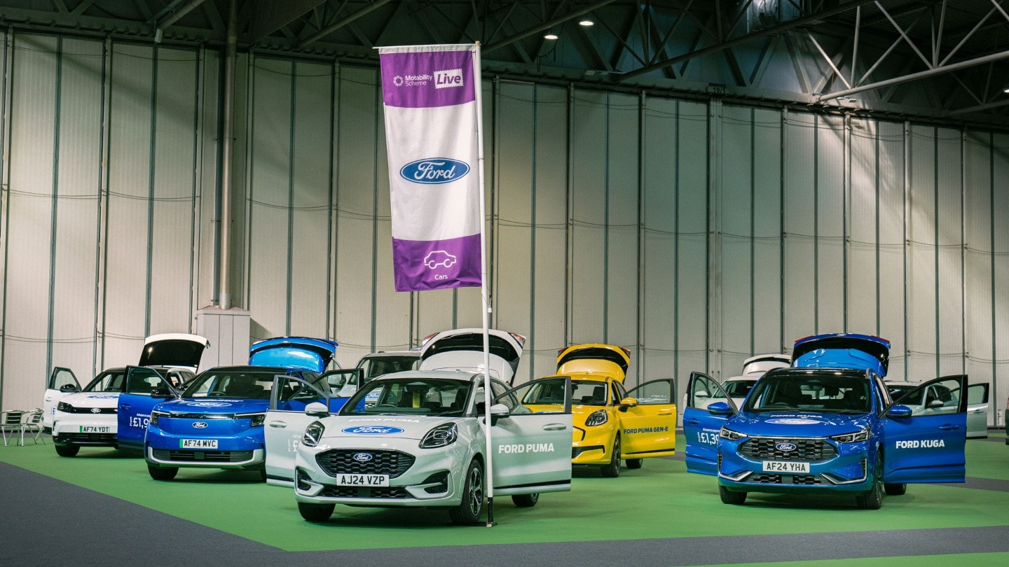 Ford vehicles (Puma, Kuga, Capri, Explorer, Gen-E) and a Ford flag at an event with open doors.