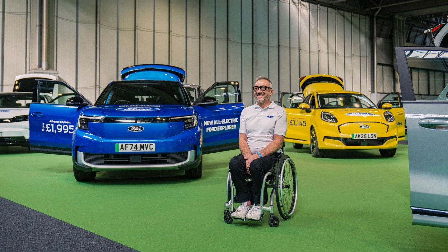 Jason Richards in a wheelchair with a blue Ford Explorer and a yellow Ford Puma Gen-E at an event.