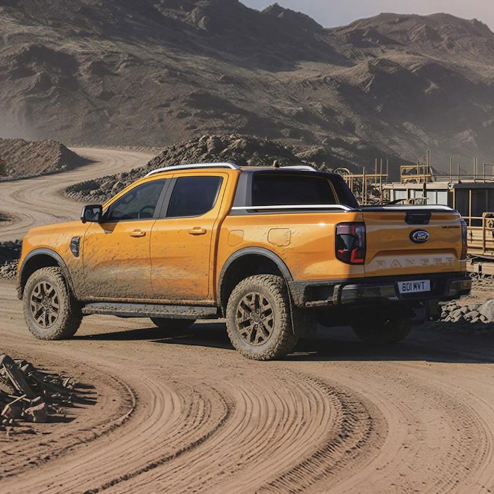 Orange Ford Ranger pickup truck on a dirt road at a construction site.