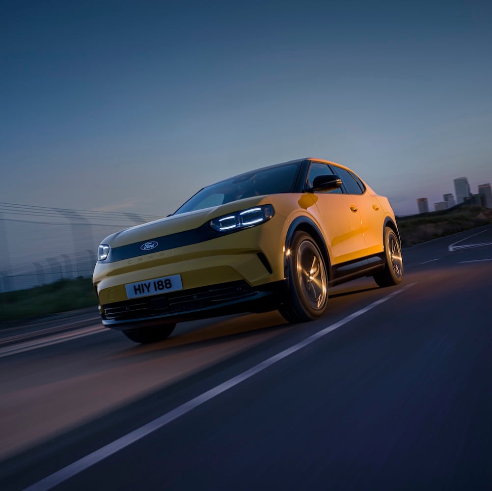 Yellow Ford Capri driving on a road at sunset.